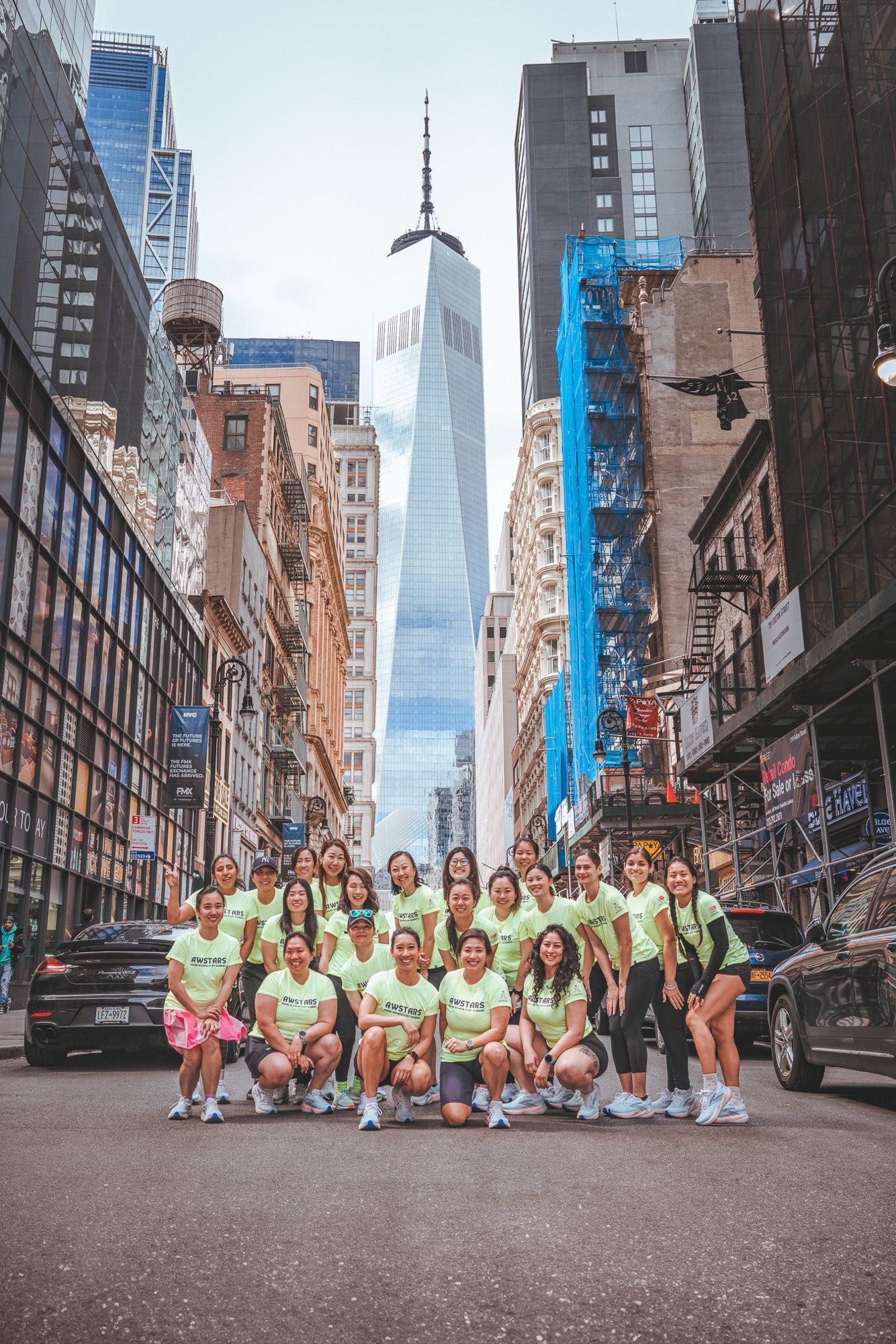 A run club posed in the middle of a downtown street with One World Trade Center rising behind them