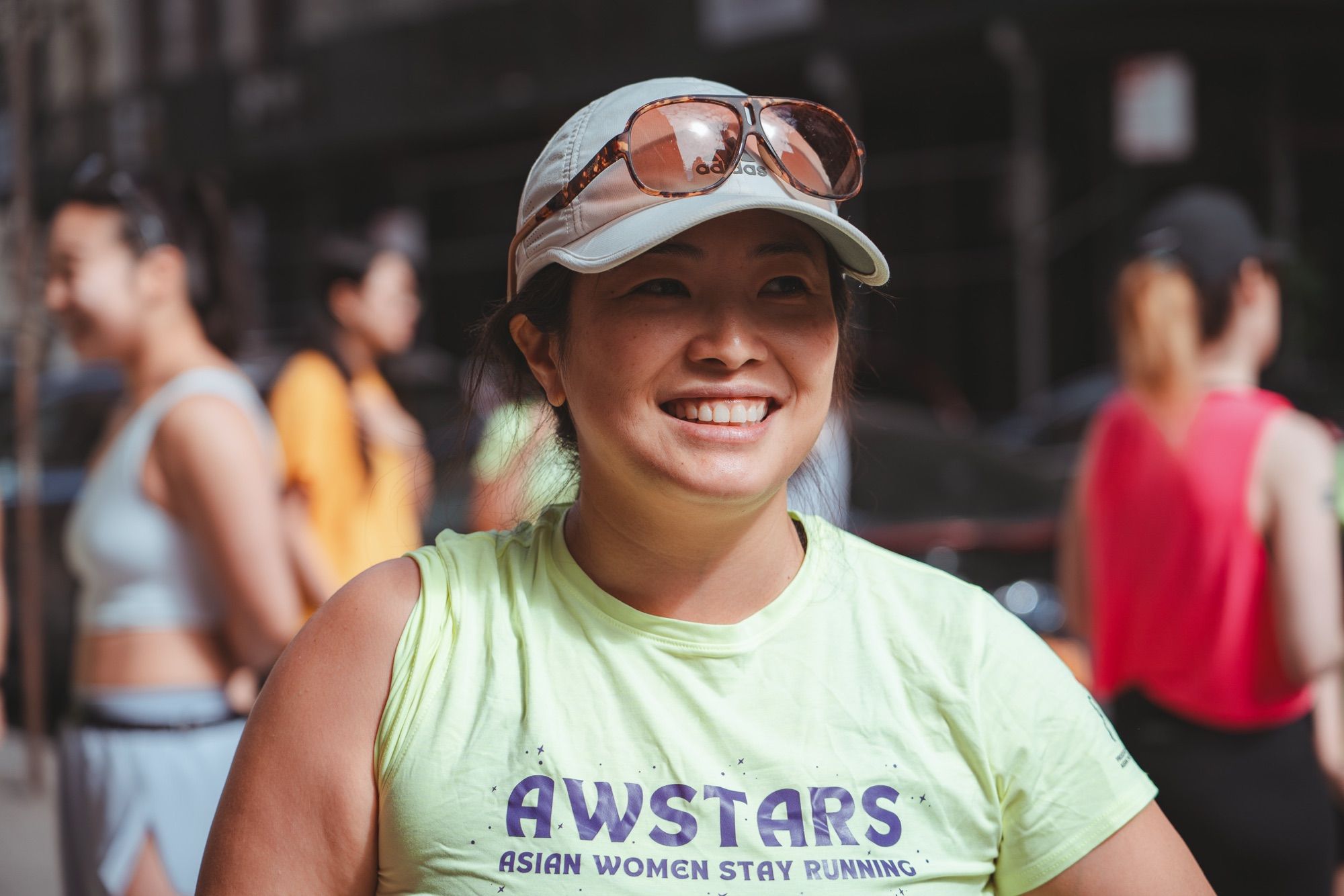 A runner in an AWSTARS shirt and cap laughing, other runners blurred behind her