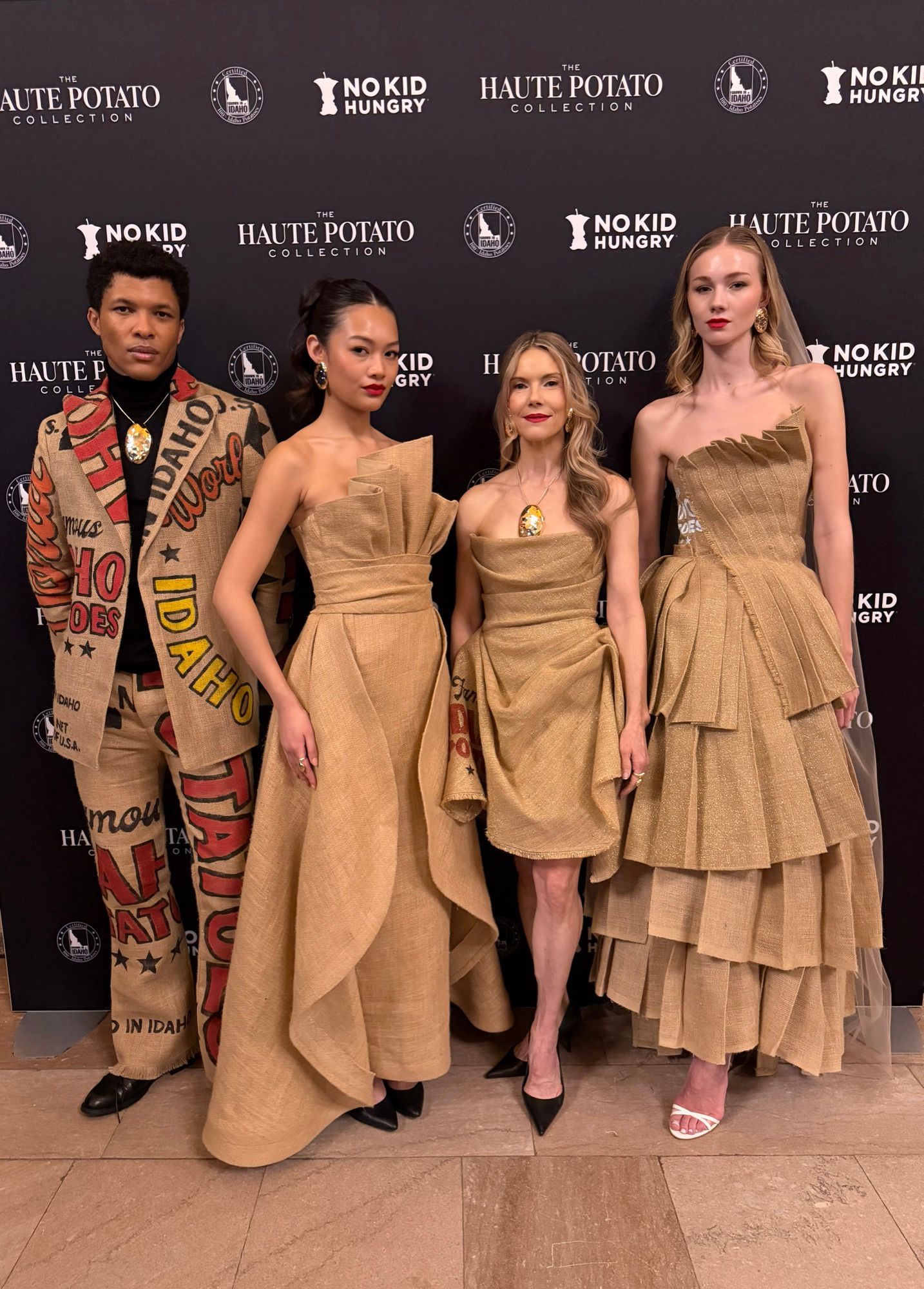 Four models in tan outfits posed on a step and repeat at a fashion event