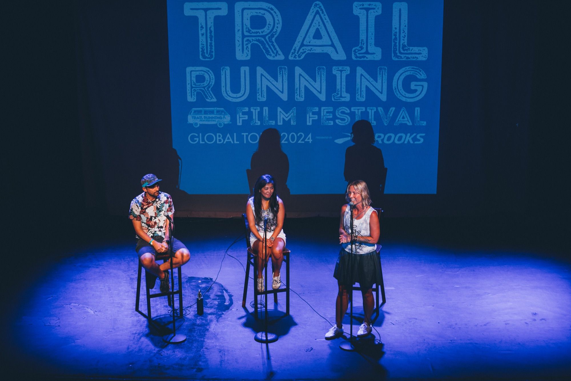 Three panellists on stools in front of a Trail Running Film Festival screen